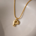 The Bubble Letter Necklace in 18K Gold showcases a shiny, chunky letter P charm pendant on a smooth, light surface—an elegant piece of personalized jewelry.