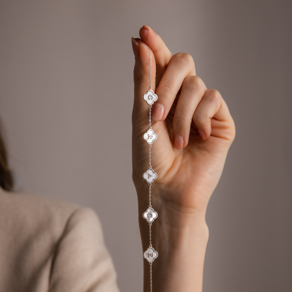 A hand holds the Pearl Clover Letter Bracelet in Sterling Silver, featuring delicate floral-shaped mother of pearl charms, against a neutral background.