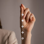 A hand holds the Pearl Clover Letter Bracelet in Sterling Silver, featuring delicate floral-shaped mother of pearl charms, against a neutral background.
