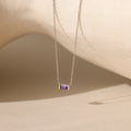 A silver Emery Birthstone Necklace featuring a rectangular amethyst gemstone, styled against a neutral-toned backdrop.