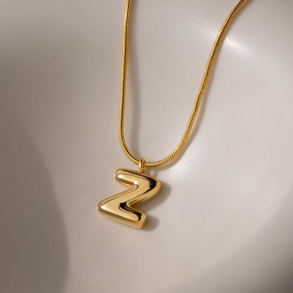 The Bubble Letter Necklace in 18K Gold features a shiny, bold Z pendant displayed on a smooth, light background—perfect for personalizing your style or making a statement with bubble letter jewelry.