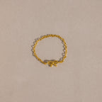 A delicate gold chain ring with a small, polished bow charm placed neatly on a soft beige background.