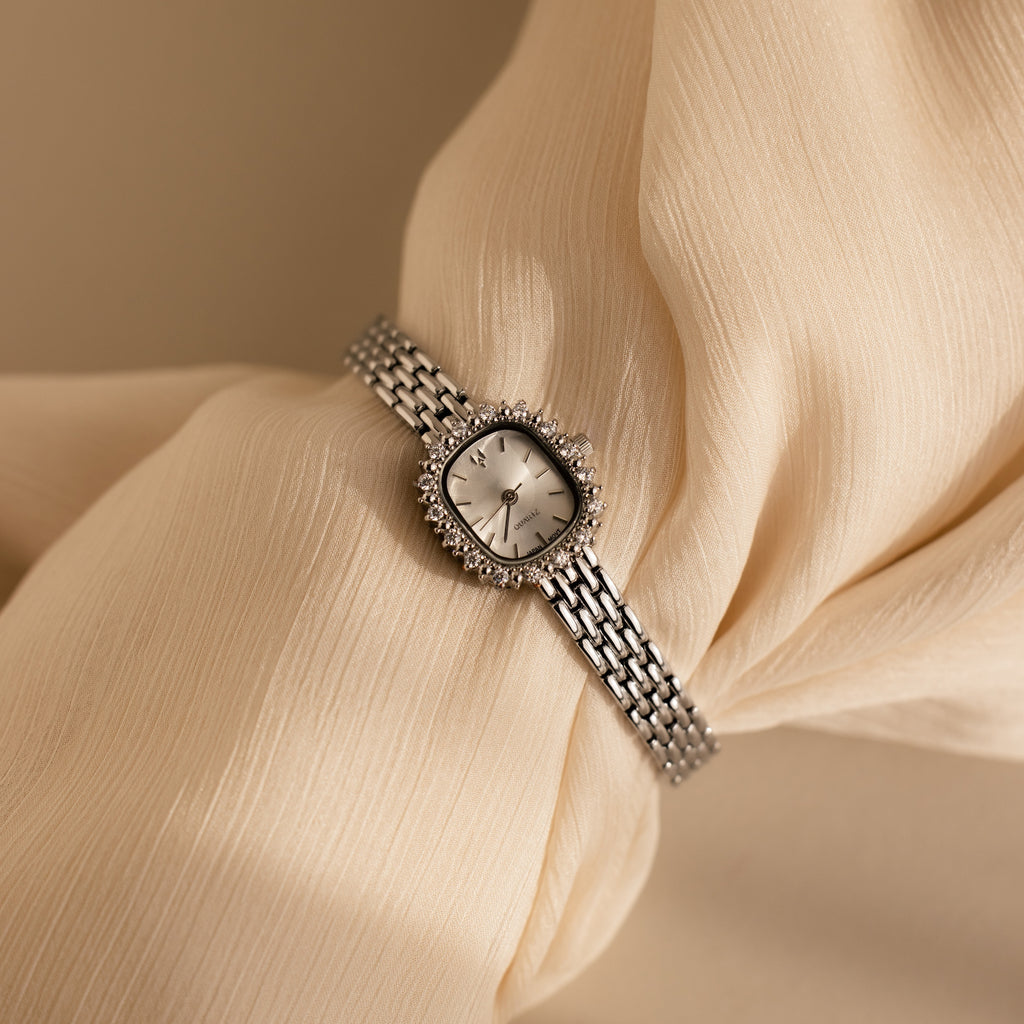The Pave Blossom Timepiece is an elegant womens watch with a round face and metal band, showcased on soft cream-colored fabric for timeless appeal.