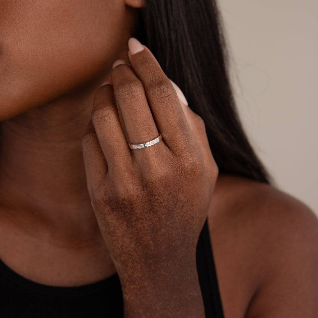 A woman wearing the Ann Thin Message Ring in Sterling Silver on her finger, holding her hand near her face.