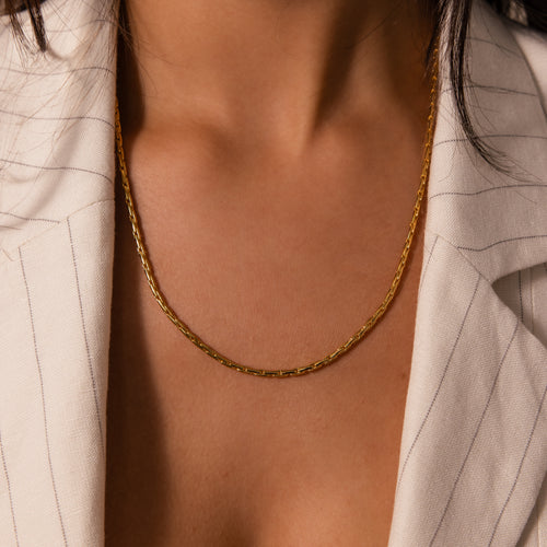 A woman in a cream pinstriped blazer showcases the Bold Link Chain Necklace in 18K Gold, styled from shoulders to chest for a modern statement look.