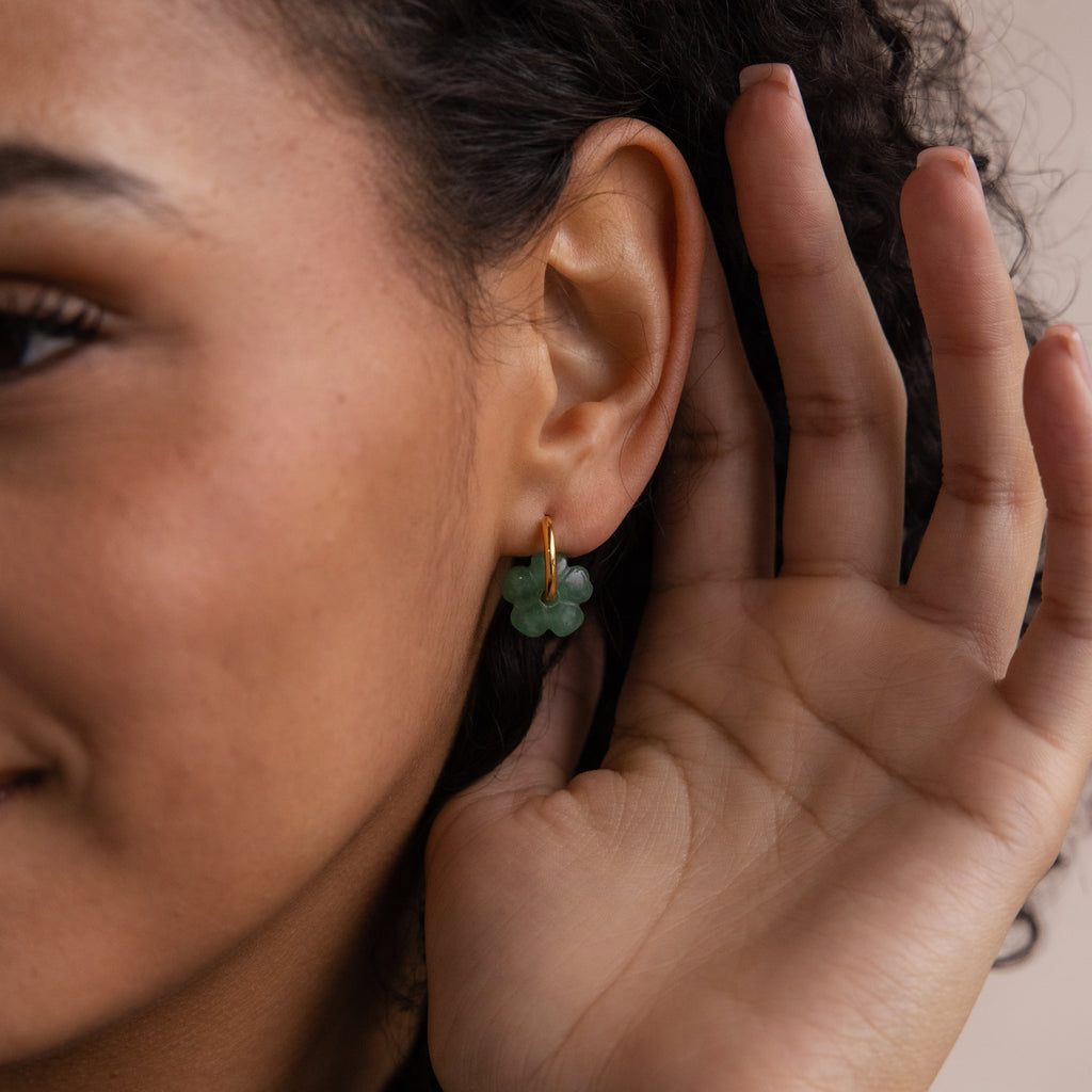 A person touches their ear, wearing Jade Flower Hoops—dainty gold hoops featuring a green jade flower, perfect as a meaningful gift.
