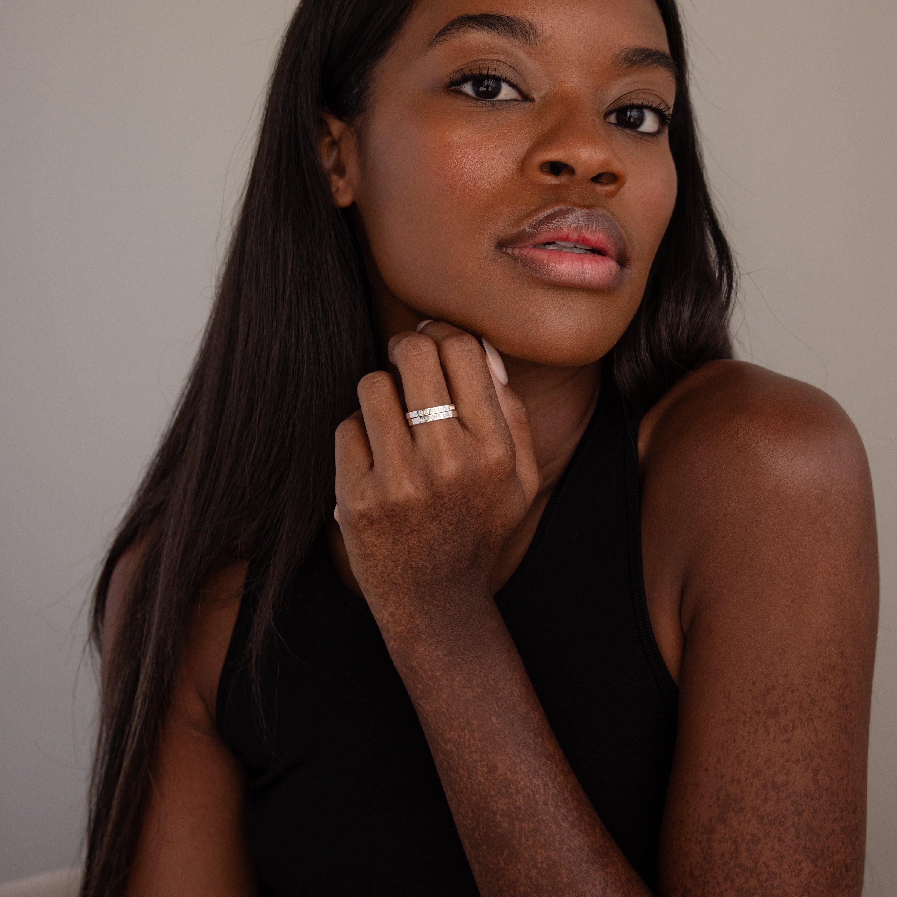 A woman with long hair in a black top confidently displays the Ann Thin Message Ring in Sterling Silver on her hand while looking directly at the camera.