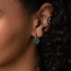 Close-up of an ear wearing Jade Flower Hoops in Silver, with delicate jade flower details and curly dark hair partially visible.