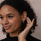 Woman with curly hair smiles, wearing Jade Flower Hoops in Silver and gently touching her ear.