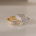 The Colette Eternity Ring in 18K Gold, set with radiant baguette diamonds, makes a stunning statement piece when displayed on a light surface.