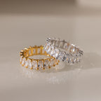 The Colette Eternity Ring in 18K Gold, set with radiant baguette diamonds, makes a stunning statement piece when displayed on a light surface.