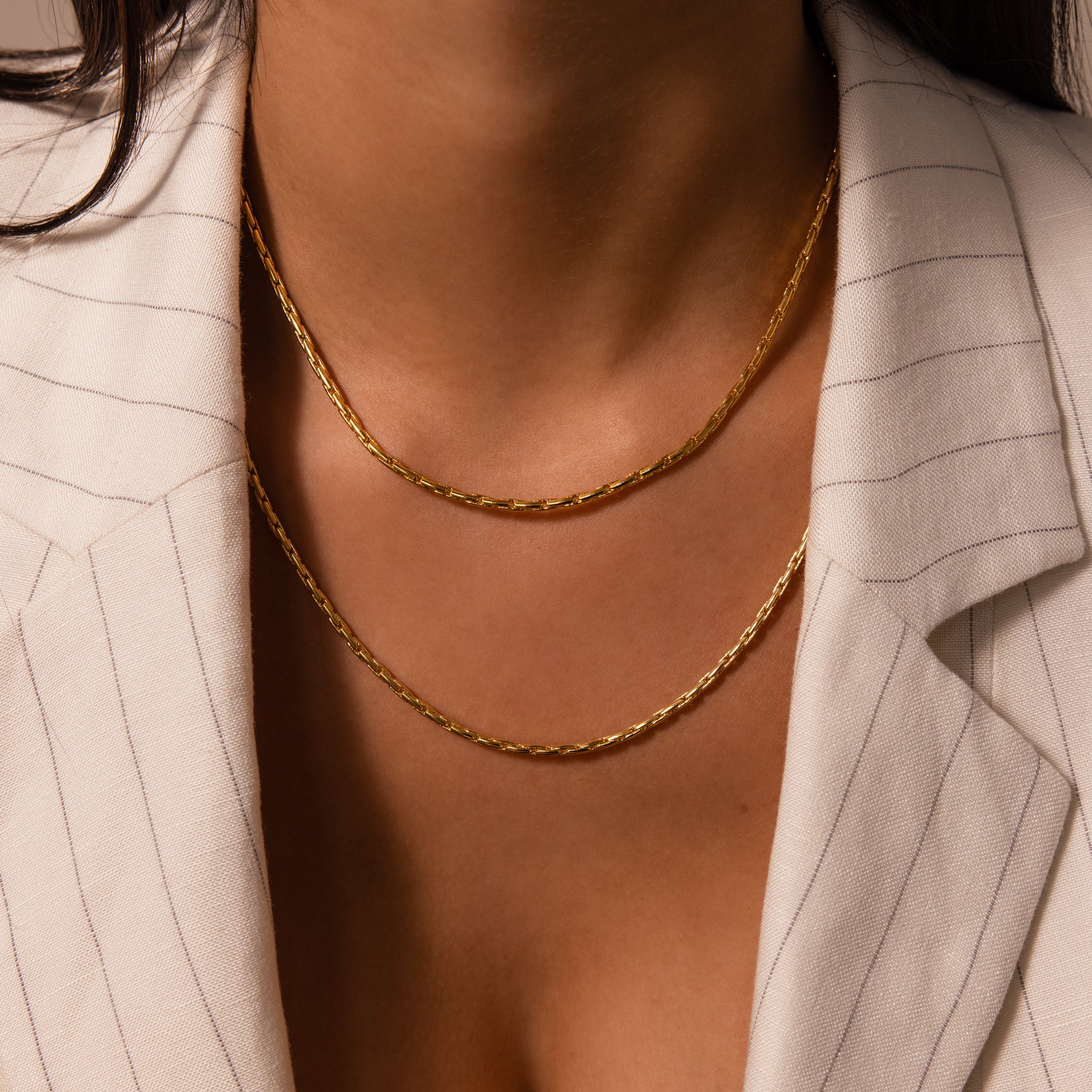 A woman in a pinstriped blazer wears two layered gold necklaces, featuring the Bold Link Chain Necklace in 18K Gold for a modern, statement look.