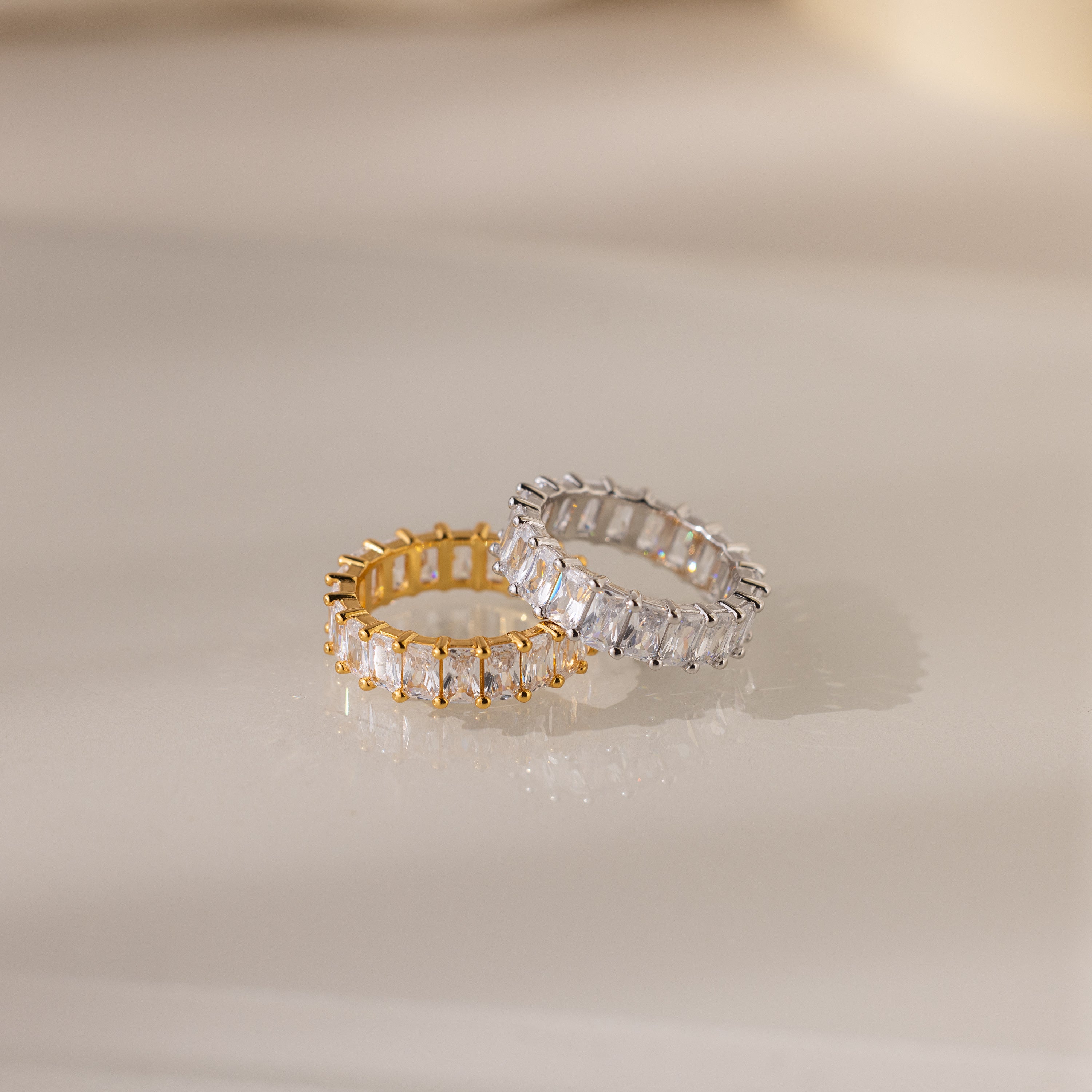The Colette Eternity Ring in Silver, adorned with sparkling baguette diamonds, shines beautifully on a glossy surface—a true statement jewelry piece.