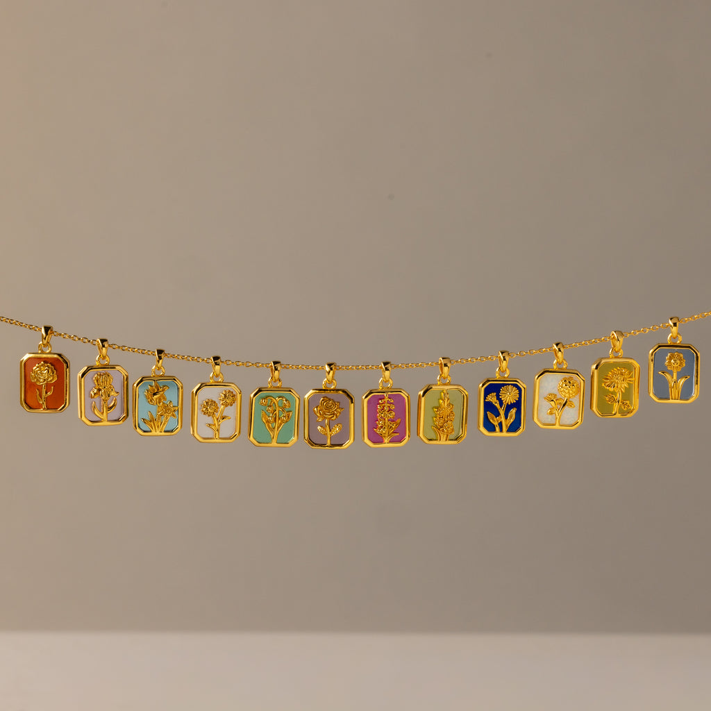 The Birth Flower Charm Necklace features a gold chain with twelve rectangular pendants, each showcasing a distinct colorful floral design—an elegant piece that brings artistic flair to any outfit.