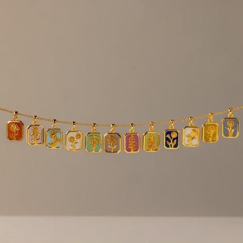 The Birth Flower Charm Necklace features a gold chain with twelve rectangular pendants, each showcasing a distinct colorful floral design—an elegant piece that brings artistic flair to any outfit.