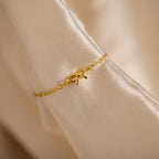 Close-up image of a delicate gold chain ring with a small bow charm in the center, elegantly draped over a folded satin fabric.