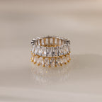 The Colette Eternity Ring, crafted in gold and silver with two rows of rectangular baguette diamonds, is displayed on a reflective beige surface.