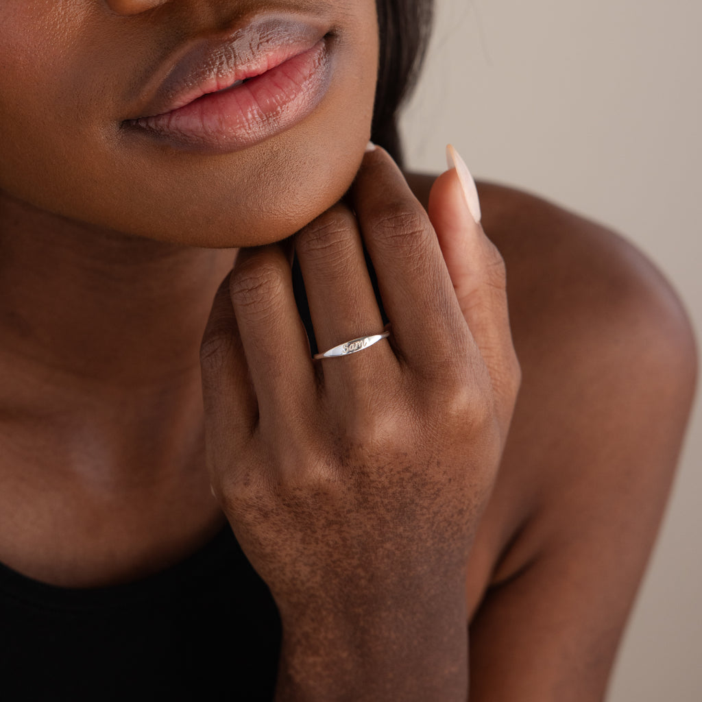 A woman gently touches her face, displaying the Ann Skinny Name Ring in Sterling Silver on her finger—the perfect Christmas gift for her.