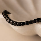 A close-up of the Onyx Tennis Bracelet, featuring black CZ diamonds, displayed on a white textured surface.
