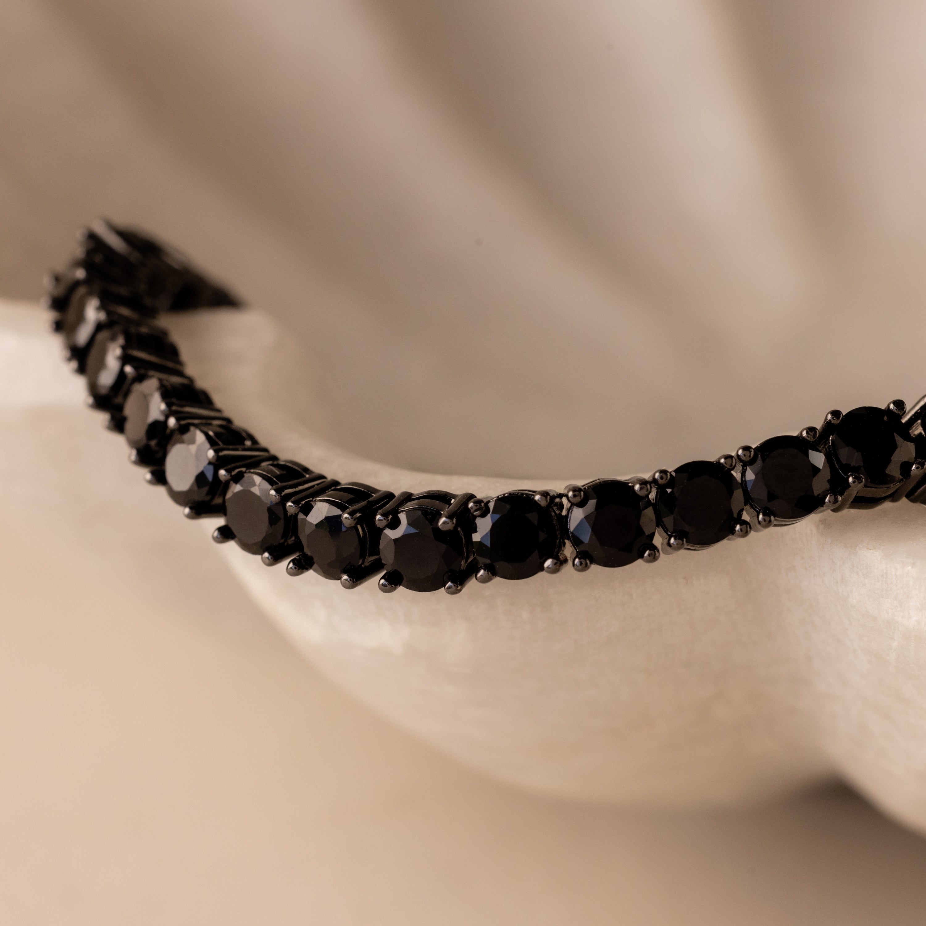 A close-up of the Onyx Tennis Bracelet, featuring black CZ diamonds, displayed on a white textured surface.