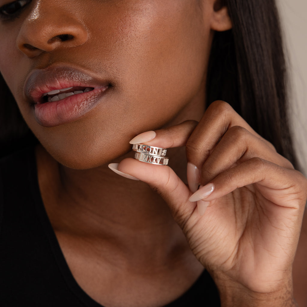 A woman holds two Roman Numerals Rings with custom engravings close to her lips, showing off her manicured nails.