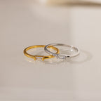 Two Baguette Diamond Rings, one gold and one silver, each with a slim band and small rectangular diamond in an east-west setting, rest on a light surface.