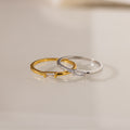 Two Baguette Diamond Rings—one gold, one silver—each with a dainty baguette diamond in an east-west bezel setting on a smooth band.