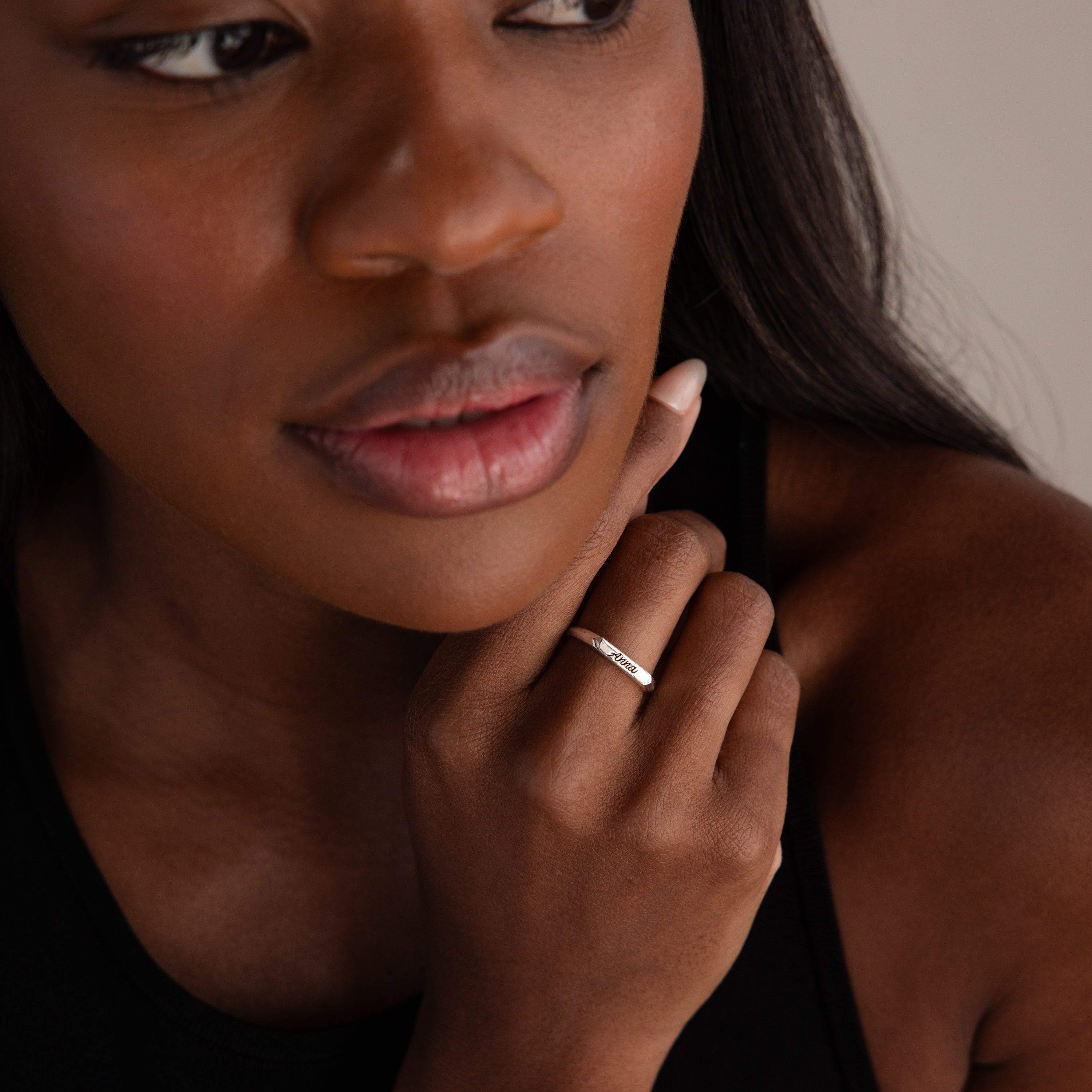Close-up of a woman touching her chin, wearing a black top and the Paris Thin Name Signet Ring in Sterling Silver on her finger.