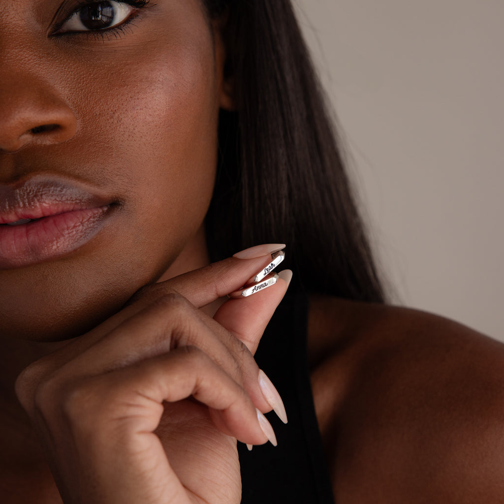 A woman holding the Paris Thin Name Signet Ring in Sterling Silver near her face, highlighting her manicured nails and smooth skin.