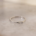 The Baguette Diamond Ring in Silver showcases a dainty baguette diamond set east-west in an elegant bezel setting, displayed on a light marbled surface.