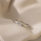 The Baguette Diamond Ring features a delicate silver band and rectangular east-west set stone, elegantly displayed on soft, creamy fabric.