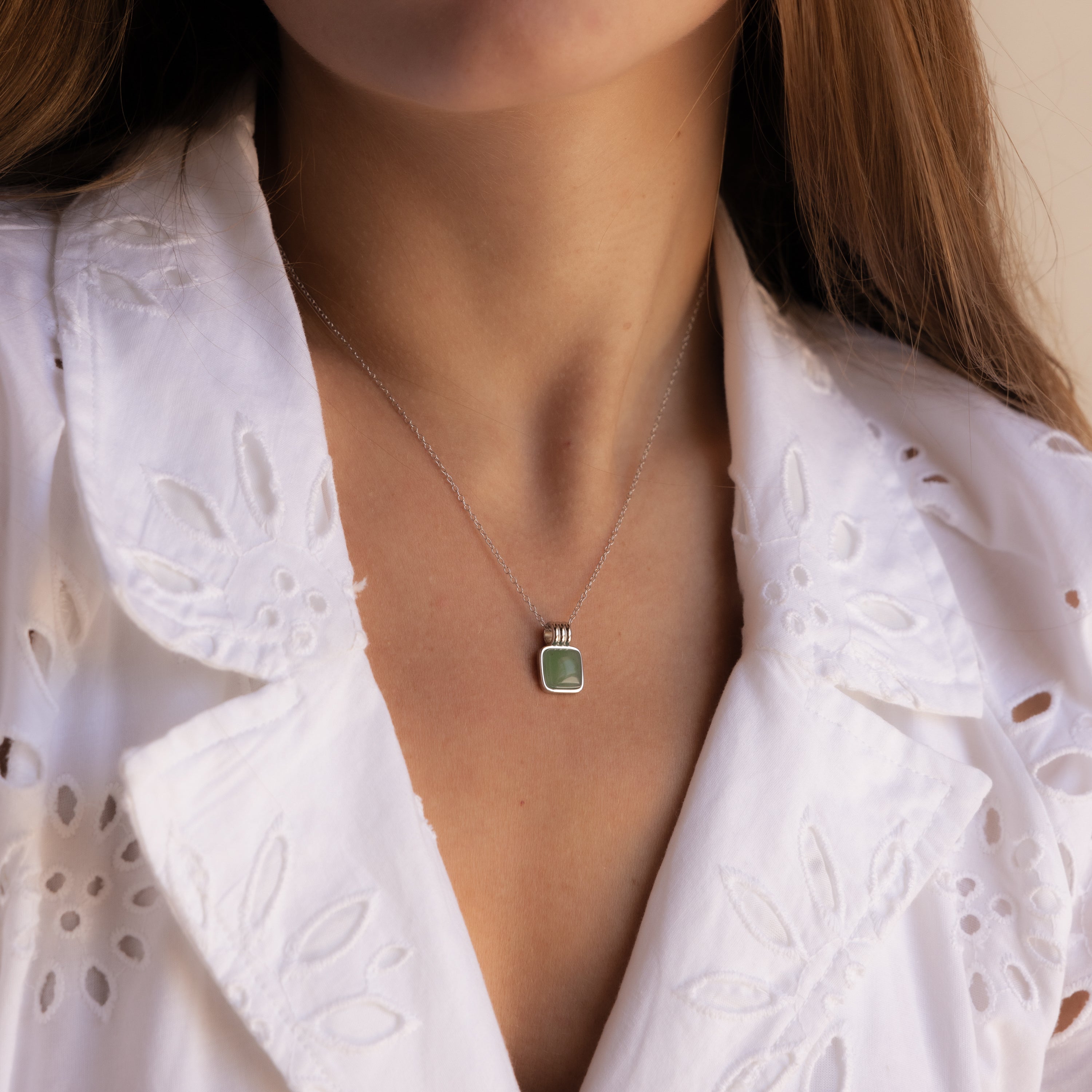 Woman wearing a white embroidered blouse and a Jade Pendant Necklace in Silver, featuring a green jade stone believed to bring luck.