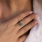 A person wearing a Jade Pendant Necklace in Silver, featuring a shimmering green jade stone, holds it near their collarbone for luck.