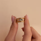 Moss agate ring stacked with three other gold bands, including pavé and domed styles, held between two fingers against a soft beige background.