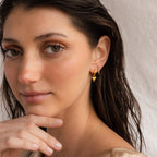 A woman with wet hair wears Shark Tooth Huggies, gazing at the camera with her hand by her chin—a laid-back look ideal for your next beach getaway.