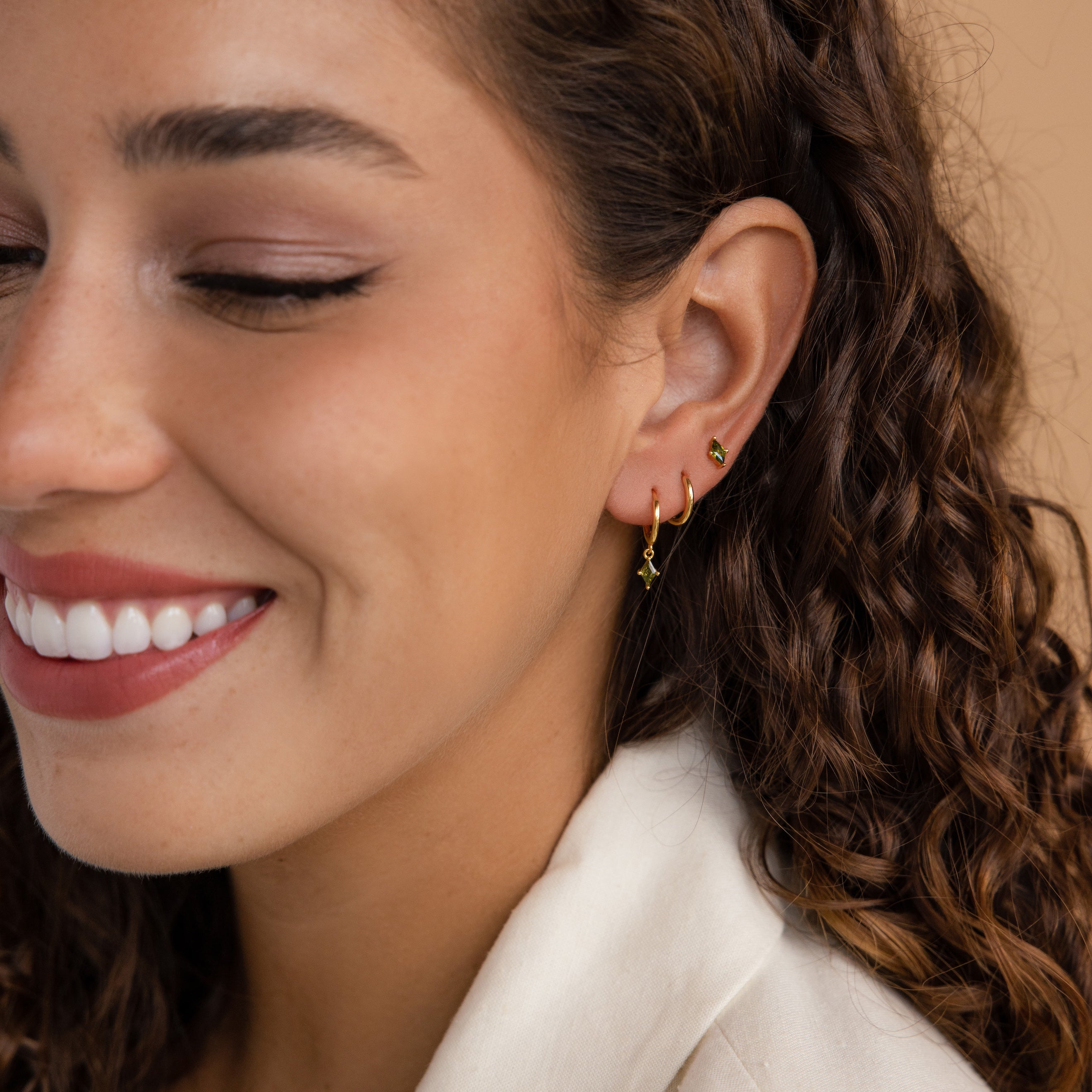Close-up of a smiling woman with curly hair wearing Peridot Earrings Set in 18K Gold and a white blazer.