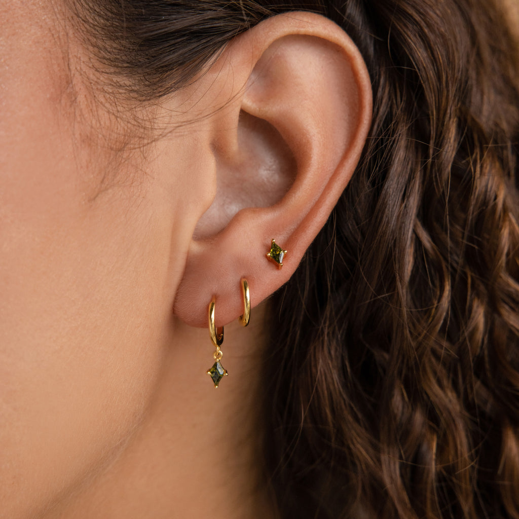Close-up of a woman's ear wearing the Peridot Earrings Set: a small gold stud paired with a delicate gold hoop earring featuring a peridot gemstone charm.