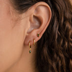 Close-up of a woman's ear wearing the Peridot Earrings Set: a small gold stud paired with a delicate gold hoop earring featuring a peridot gemstone charm.