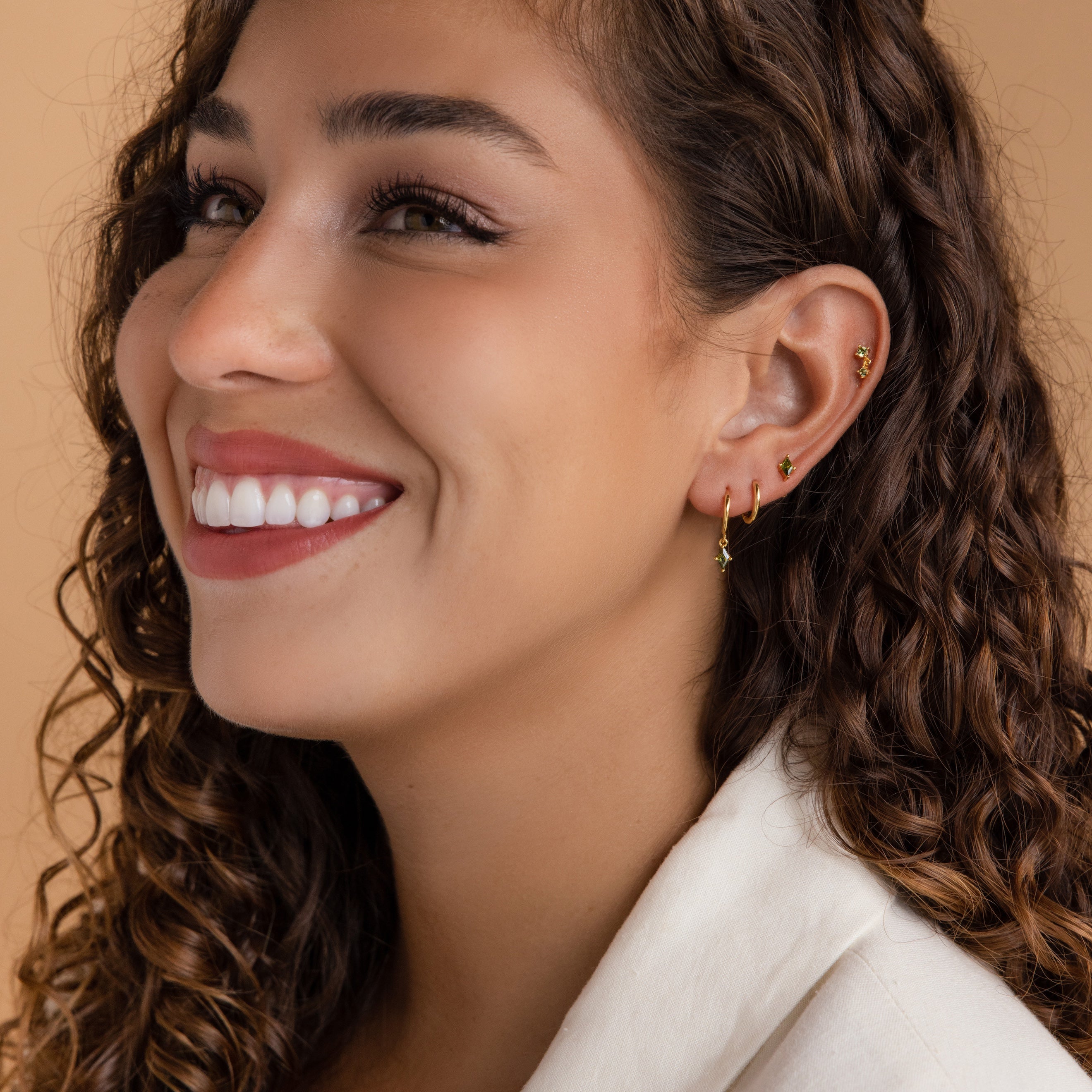 Smiling woman with curly hair wearing the Peridot Earrings Set and a beige top, shown in side profile.