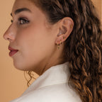 Woman with curly brown hair, facing sideways, wears the Peridot Earrings Set in 18K Gold—including a delicate cartilage earring—with a white blazer.