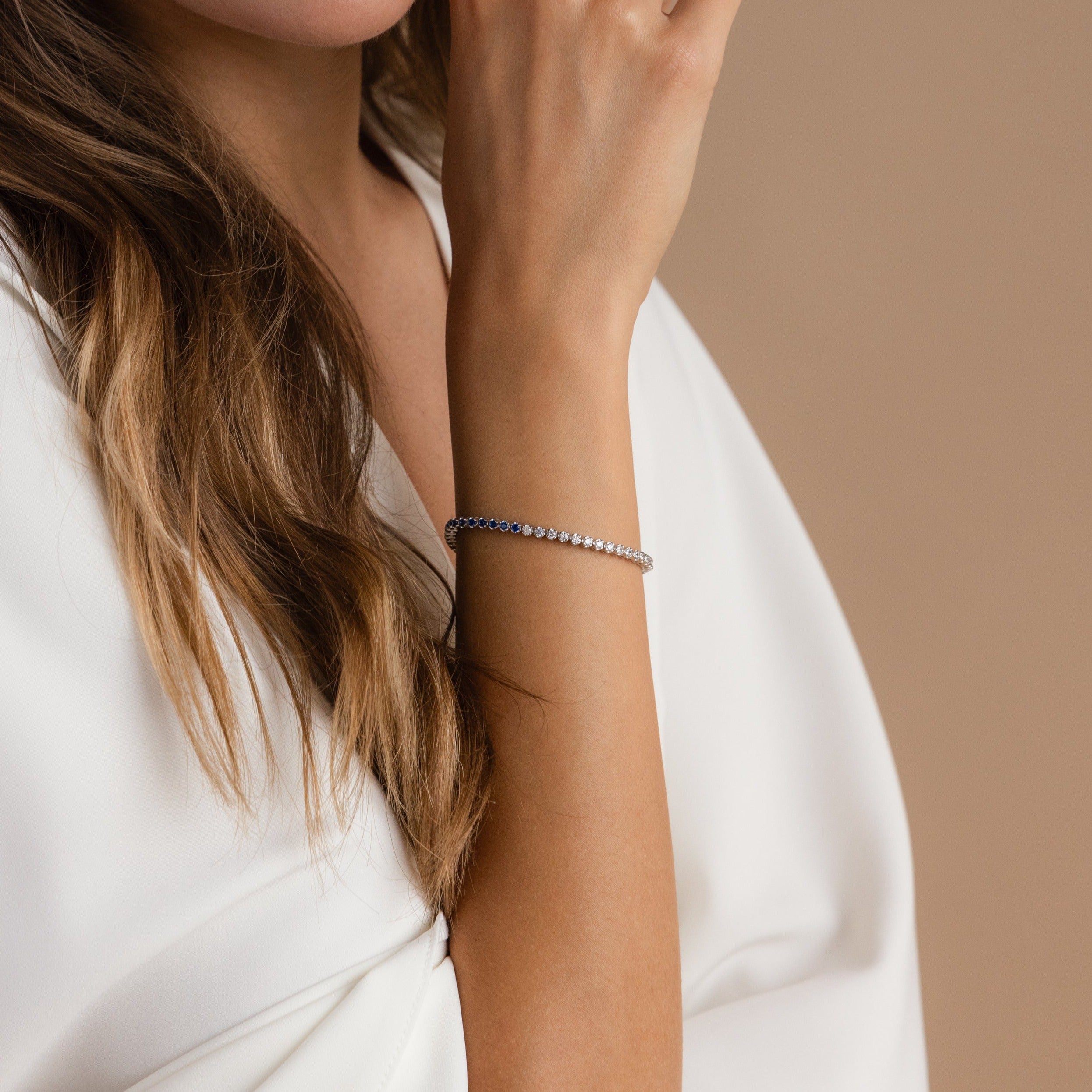A woman wears the Blue Diamond Tennis Bracelet on her wrist with a white blouse, set against a neutral background.