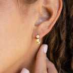 Close-up of a woman's ear wearing gold Triple Blue Zircon Huggies with three blue zircons, hand near her ear—perfect customizable gemstone earrings for a minimalist look.
