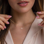 A woman with pink nails holds the delicate Opal Butterfly Necklace Set near her neck, showcasing its small butterfly pendant.
