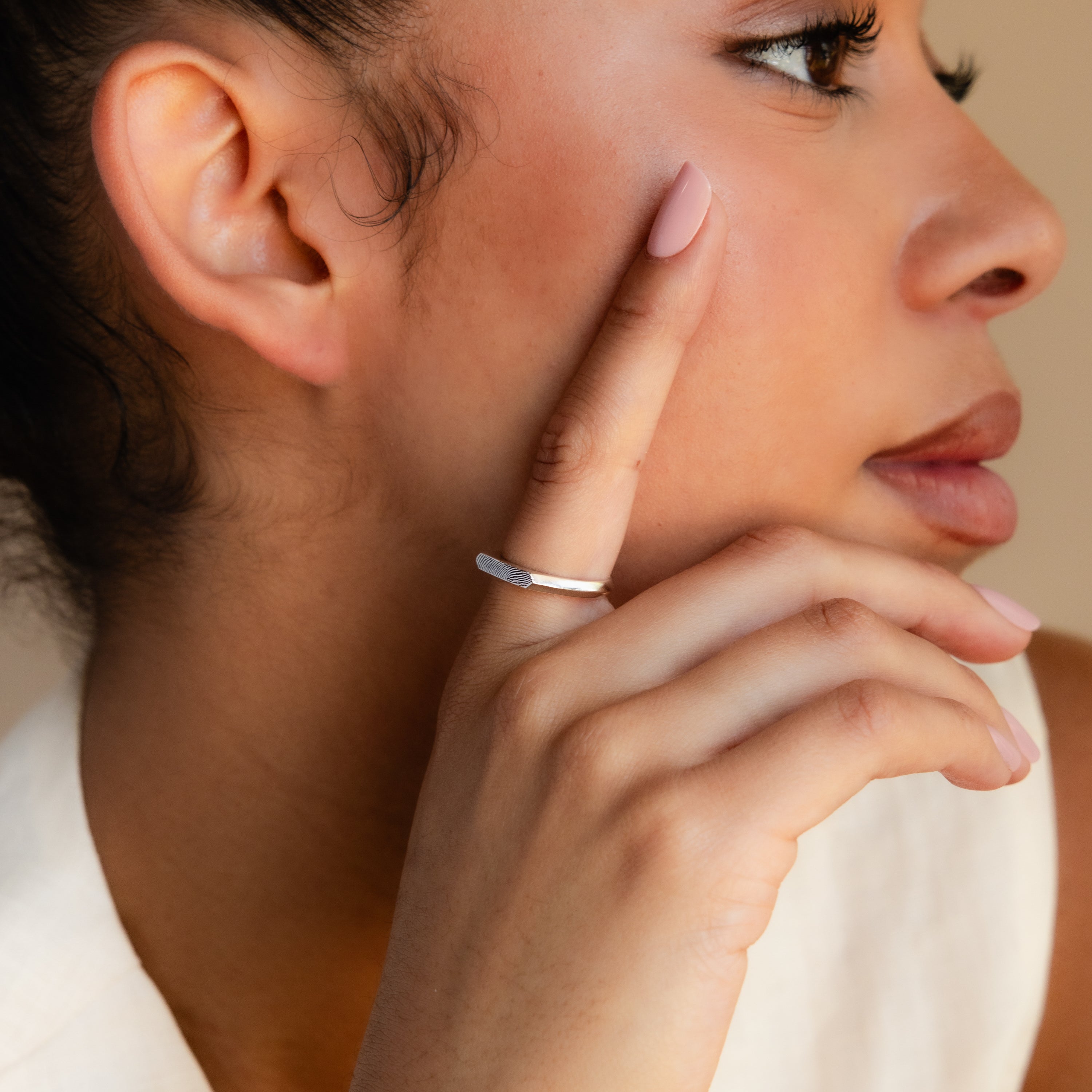 A woman with manicured nails touches her face, wearing the Thin Fingerprint Signet Ring in silver on her index finger as she looks sideways.