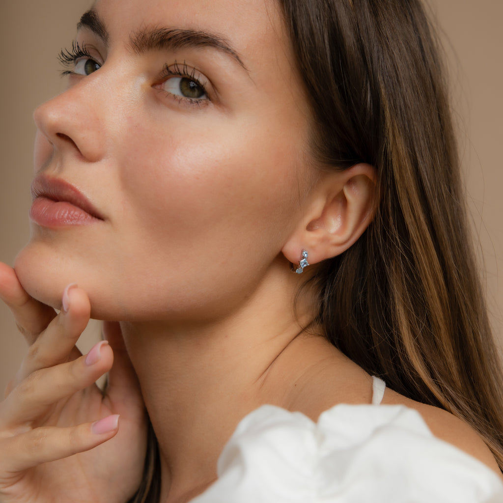 Model wearing silver Aquamarine Hoop Earrings while touching her face