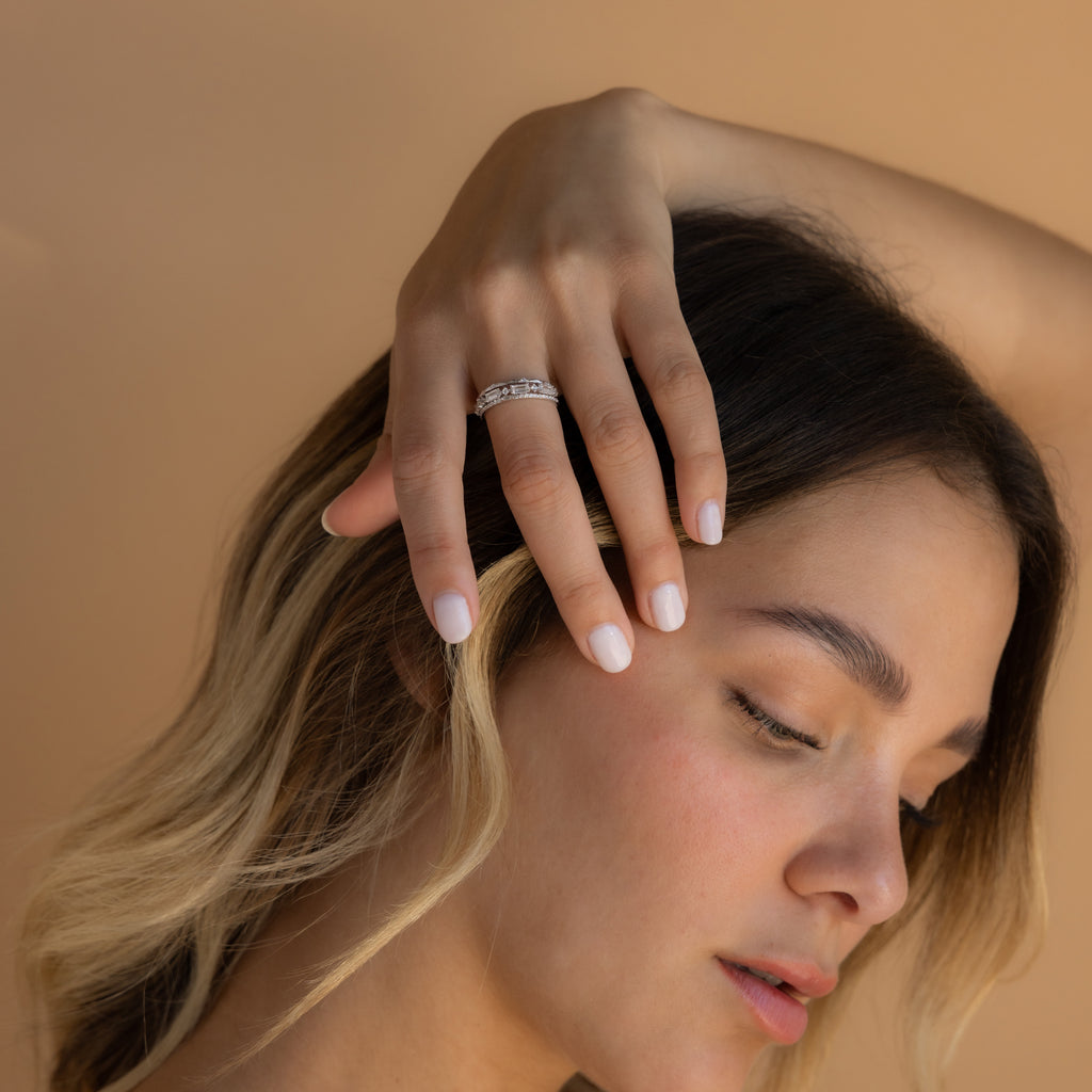 A woman with light nails displays the Diamond Stacking Ring Set in Sterling Silver on her hand against a beige background—an elegant Christmas gift choice.