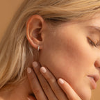 A side profile of a woman wearing one of the silver huggie earrings