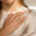 A woman with long nude nails wears the Delicate Pearl Diamond Ring, gently touching her chest over a cream-colored blouse.