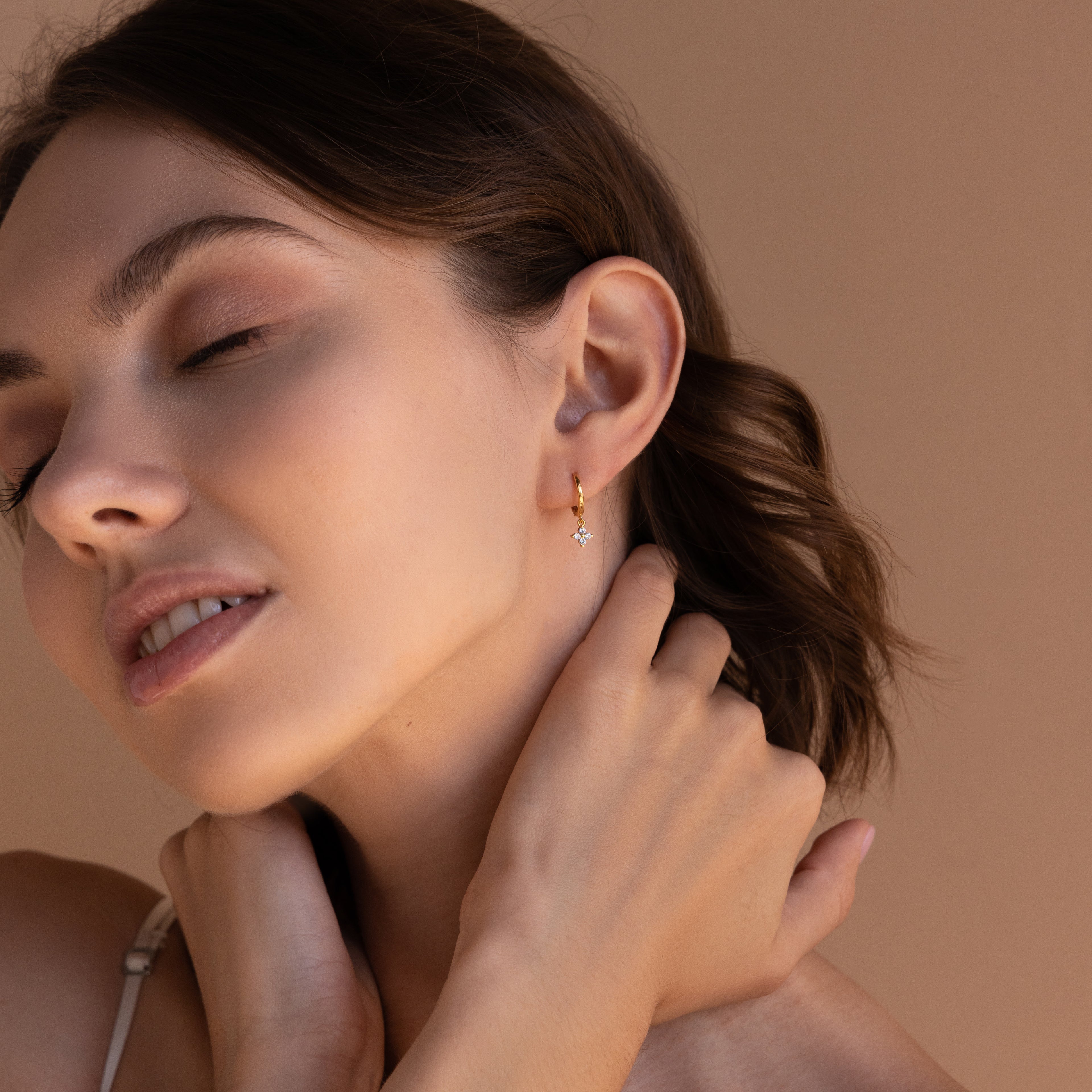 A close-up side profile of a woman wearing a gold Diamond Flower Huggie earring. 