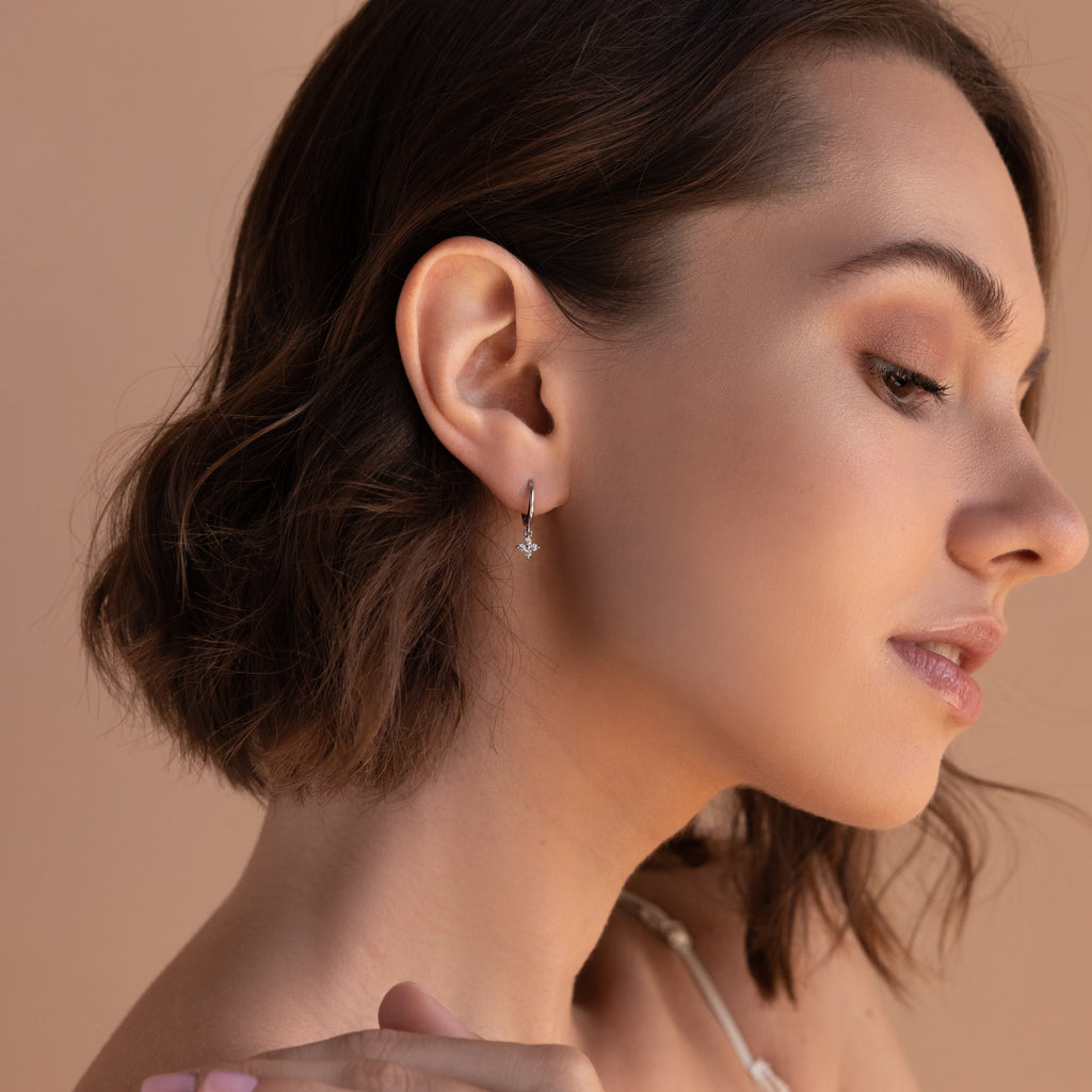 A woman poses with her head turned to the side, wearing a silver Diamond Flower Huggie